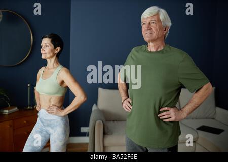 Seniorinnen und Senioren trainieren in einem gut beleuchteten Raum mit dunkelblauen Wänden und fühlen sich selbstbewusst und konzentriert. Szene fängt einen aktiven Moment ein, der Fitness und gesunden Lebensstil betont Stockfoto