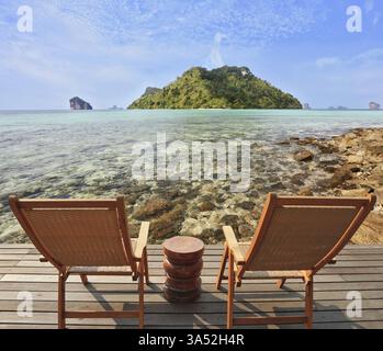 Zwei bequeme Klappstühle aus Holz und ein kleiner Beistelltisch. Durch das smaragdgrüne Meerwasser sichtbare Steine. Romantische Ecke am Südufer von t Stockfoto