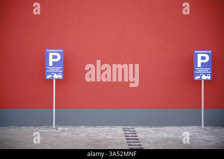 Ein Parkschild und ein Warnschild für unbefugtes Parken an einer markanten roten Wand eines Wohn- und Geschäftsgebäudes Stockfoto