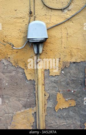 Ein stillgelegter und alter Stromverteilerkasten mit gerissenen Kabeln an einer Wand mit abblätterndem Putz Stockfoto