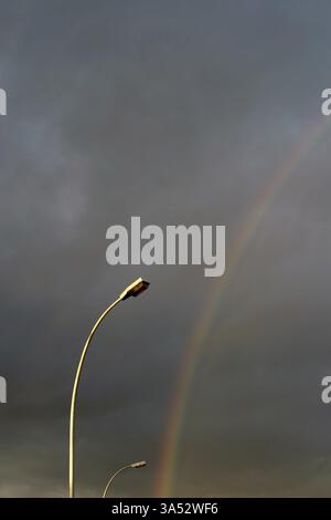 Ein Regenbogen leuchtet am Abendhimmel neben zwei Straßenlaternen Stockfoto