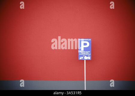 Ein Parkschild und ein Warnschild für unbefugtes Parken an einer markanten roten Wand eines Wohn- und Geschäftsgebäudes Stockfoto