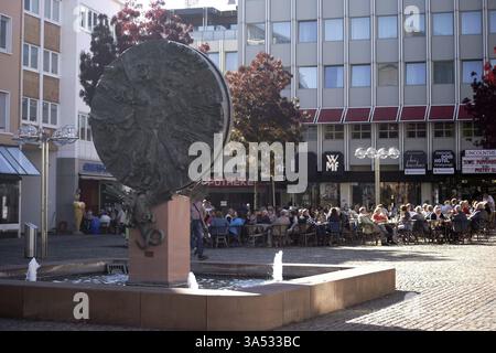 Worms, Deutschland - 13. Oktober 2018: Ein gut besuchtes Café auf dem Obermarkt mit der Skulptur Schicksalsrad des Künstlers Gustav Nonnenmacher am 13. Oktober Stockfoto