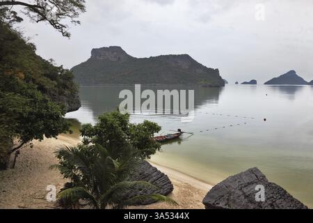 Thailändisches Longtail-Boot an einem Sandstrand mit Anker. Malerische Bucht auf der Insel, umgeben von Inseln. Nebeliger Morgen nach einem schweren Sturm Stockfoto