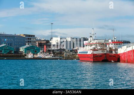 Reykjavik, Island - 4. April 2017: Ein landschaftlich reizvoller städtischer Hafen mit lebhaften Gebäuden, roten Booten am Dock und klarem blauem Himmel, der eine ruhige und friedliche Atmosphäre schafft Stockfoto