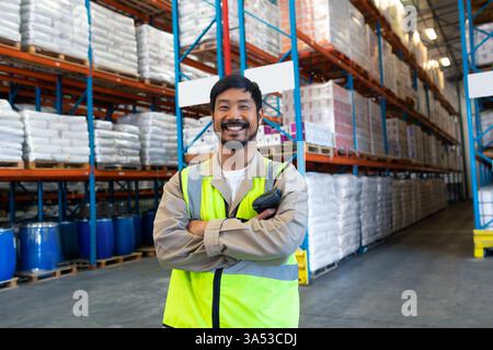 Im Lager steht der Arbeiter selbstbewusst mit überkreuzten Armen zwischen den Regalen Stockfoto