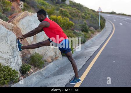 Sportlicher Mann, der sich am Straßenrand ausdehnt, sich auf den Lauf im Freien in der Natur vorbereitet, Kopierraum Stockfoto