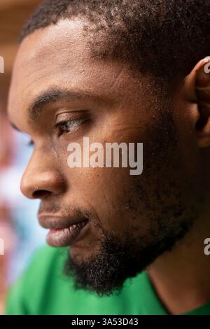 Nachdenkliche, stimmungsvolle Person mit fokussiertem Ausdrucksdenken, Seitenprofil Nahaufnahme. Detaillierte Aufnahme eines afroamerikanischen erwachsenen Mannes drinnen mit reflektierendem Blick auf das Gesicht Stockfoto