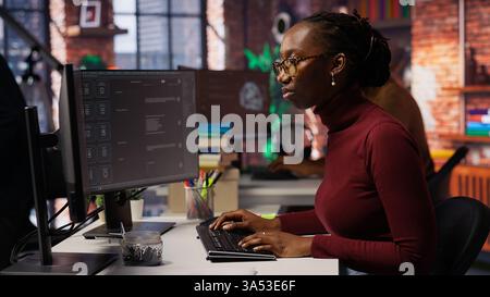 IT-Startup-Mitarbeiter verwenden eine Anwendung mit großem Sprachmodell, um Hilfe bei Programmieraufgaben zu erhalten. Frau interagiert mit KI LLM Chatbot PC GPT Software auf PC in Software-Entwicklung Arbeitsplatz, Kamera B Stockfoto