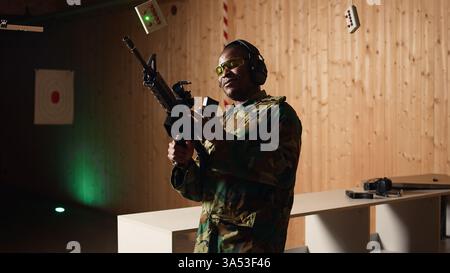 Porträt eines fröhlichen Soldaten, der auf dem Schießstand trainiert, Gewehr nachlädt. Fröhliche Militäreinheit im Schießstand, die mit halbautomatischen Waffen übt, Schutzausrüstung trägt, Kamera A Stockfoto