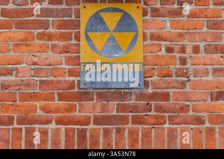Ein altes gelbes silbernes Fallout-Schutzschild an der roten Ziegelwand Stockfoto