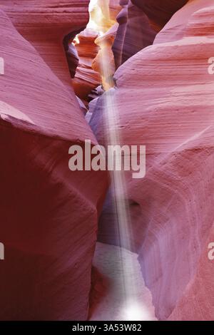 Mittag in einem rot-Orange Antelope Canyon. Ein dünner Strahl des Tageslichtes leuchtet auf dem sandigen Boden des Canyons Stockfoto