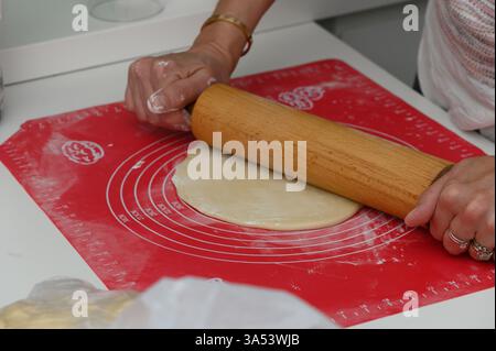 In einer modernen Küche rollt eine Person gekonnt Teig auf einer hellroten Matte aus und bereitet sich auf die Konditorei vor. Das warme Ambiente lädt zu kulinarischer Kreativität ein Stockfoto