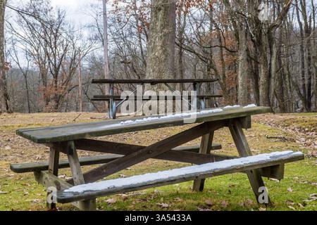 Picknicktische in einer ruhigen Waldlichtung sind leicht mit Schnee bedeckt. Stockfoto