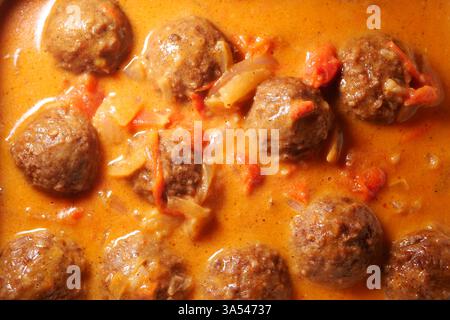 Herzhafte Fleischbällchen, die in einer reichhaltigen Tomatensauce in einer warmen Küche kochen Stockfoto