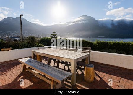 Holztisch auf der sonnendurchfluteten Terrasse mit Blick auf die Berge und das Meer, ideal zum Entspannen, Kopierraum Stockfoto
