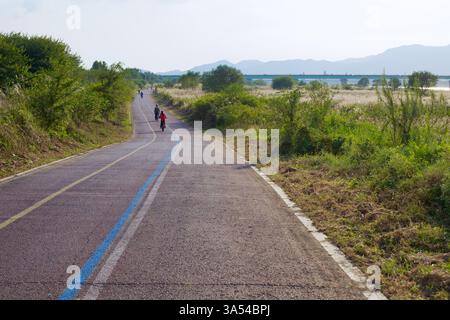 Gwangju, Südkorea - 24. September 2020: Radfahrer fahren entlang des Yeongsangang Bike Path, umgeben von üppiger Vegetation und weit entfernten Bergen, wie der Stockfoto