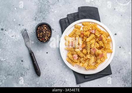 Carbonara-Pasta mit knusprigen Speckstückchen und Parmesankäse auf einem Teller. Grauer Hintergrund. Draufsicht. Stockfoto