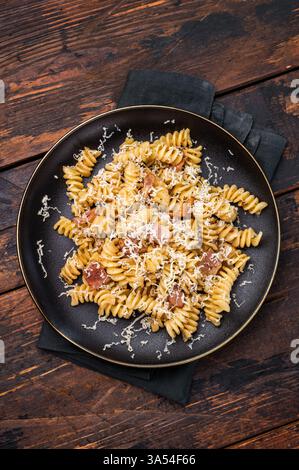 Italienische Carbonara-Pasta mit knusprigen Speckstückchen auf einem Teller. Hölzerner Hintergrund. Draufsicht. Stockfoto