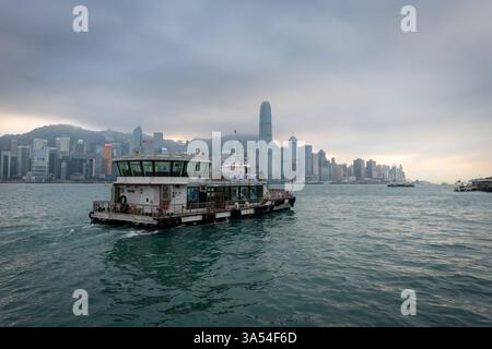 Hongkong. China- 02.20.2025. Ein Boot, das bei Sonnenuntergang auf Victoria mit berühmten Wolkenkratzern auf der Insel Hongkong im Hintergrund segelt. Stockfoto
