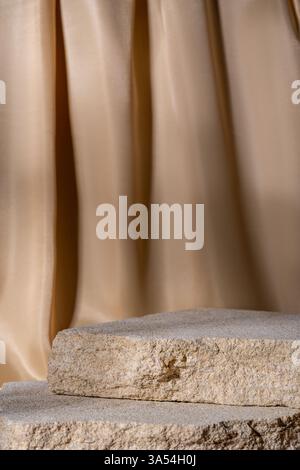 Beige Natursteine Podium auf beigem textilen Vorhang Hintergrund, Plattform für Produktpräsentation. Leer für Modelldesign. Vorderansicht. Kopierbereich Stockfoto