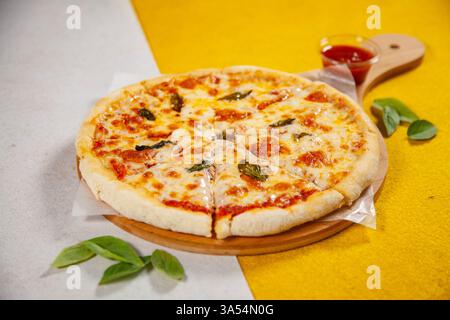 Pizza Margarita auf einem runden Holzteller mit gelbem und weißem Hintergrund. Stockfoto