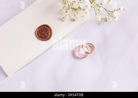Zwei goldene Eheringe liegen auf einem weißen Tüllstoff mit gypsophila-Blüten. Zarter Hochzeitsumschlag mit Stempel. Details zum Hochzeitstag der Braut Stockfoto