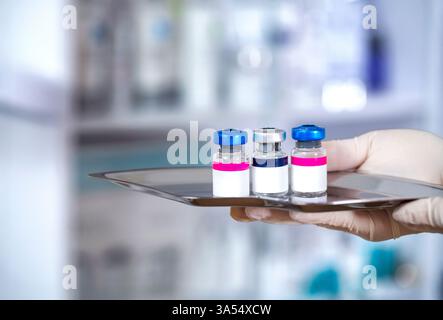 Medizinische Impfstofffläschchen mit weißem Blanko-Etikett in der Wissenschaftlerhand mit weißen Gummihandschuhen. Nahaufnahme einer Hand, die Impfstoffglasflaschen für hält Stockfoto