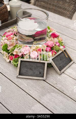 Ein wunderschönes Blumenarrangement mit Rosen, Hortensien, einer Glasvase mit schwimmender Blume und dekorativen Holzanhängern, perfekt für besondere Gelegenheiten Stockfoto