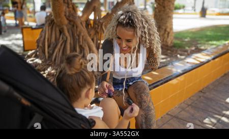 Mutter mit Tattoos und Tochter, die gemeinsam in einem urbanen Park einen verspielten Moment genießt Stockfoto