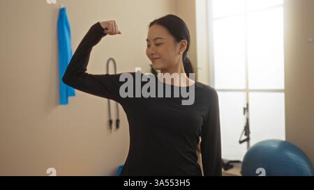 Junge chinesin, die sich in einem Fitnessstudio in schwarzer Sportbekleidung mit Fitnessgeräten im Hintergrund unter natürlichem Licht bewegte Stockfoto