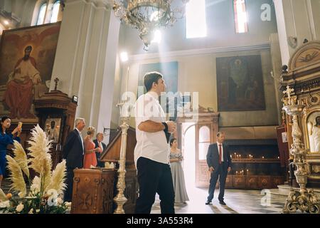 Montenegro, Kotor – 13. Juli 2024: Fotograf filmt eine Hochzeitszeremonie in einer Kirche mit Kamera auf einem Stativ. Seitenansicht Stockfoto