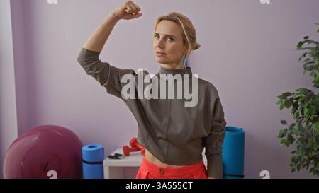 Frau beugt Arm im Fitnessstudio mit Trainingsball, zeigt Kraft und Fitness, in lässiger Trainingskleidung, in einem hell beleuchteten Sportzentrum mit Äquivalent Stockfoto