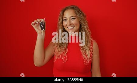Blonde Frau, die Autoschlüssel hält, lächelt über isoliertem roten Hintergrund Stockfoto