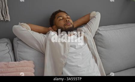 Junger Mann, der sich auf einer Couch in einem modernen Wohnzimmer entspannt und in einem ruhigen Moment drinnen ein Gefühl der Ruhe und des Komforts in einer häuslichen Umgebung zeigt. Stockfoto