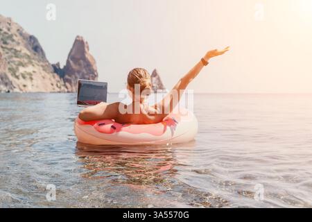 Mann, Strand, Schwimmen - Entspannen auf rosa Flamingo aufblasbarem Ring im Ozeanwasser in der Nähe von felsigen Klippen an sonnigen Tagen. Stockfoto