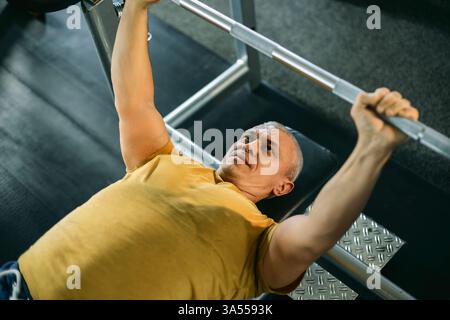 Konzentrierter Senior-Mann, der eine Langhantel im Fitnessstudio hebt Stockfoto