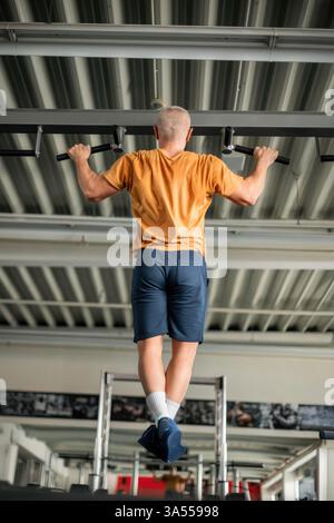 Ein Mann, der an einer Bar in einem modernen Fitnessstudio Pull-ups macht Stockfoto