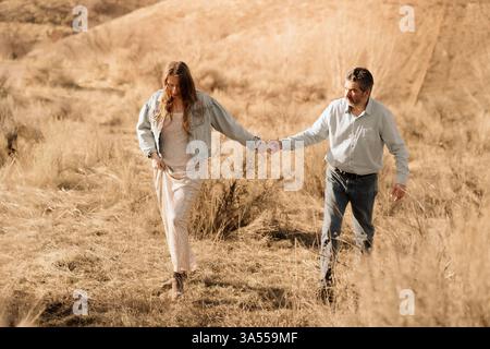 Ein Paar geht Hand in Hand und erkundet im Frühjahr ein grasbewachsenes Feld Stockfoto