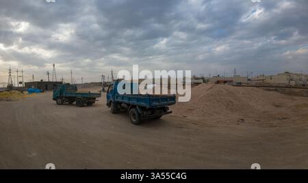 Zwei blaue LKWs parkten auf einer Sandbaustelle unter bewölktem Himmel. Stockfoto
