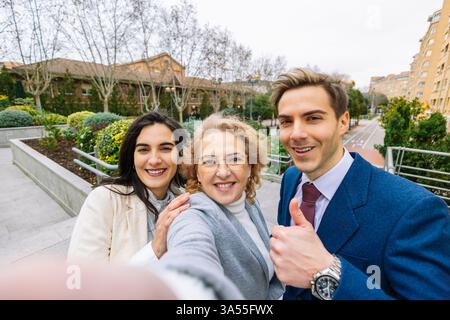 Drei selbstbewusste Profis lächeln beim Selfie in einem Stadtpark. Teamwork, Networking und positive Arbeitsbeziehungen. Lifestyle Stockfoto