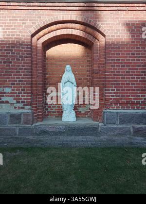 Weiße Marienstatue an der roten Backsteinmauer Stockfoto