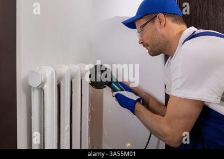 Arbeiter schneidet alten Gusseisenkühler mit Winkelschleifer ab. Renovierungsservice für Hausheizungen Stockfoto