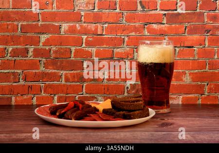 Ein Glas dunkles Bier und ein Teller mit einer Auswahl an Fleischsnacks mit Käse und Croutons. Nahaufnahme. Stockfoto