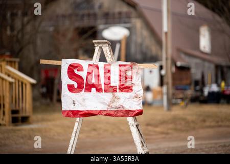 Ein großes Schild mit dem Wort „Sale“ in Rot steht auf einer Staffelei vor einem Immobilienverkauf. Stockfoto