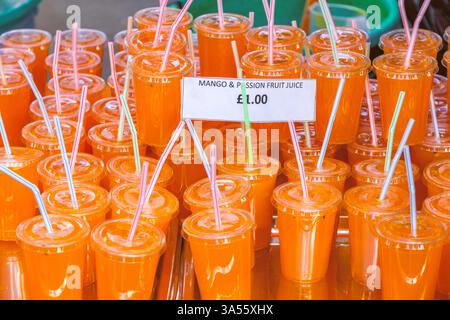 Mango- und Passionsfruchtsaft in Plastikbechern mit Trinkhalmen auf dem Brick Lane Market in London Stockfoto