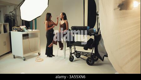 Fotografie, Backstage und Model mit Make-up-Künstler im Studio für Produktion, Vorbereitung oder Fotoshooting. Kreativ, medial und weiblich mit Stockfoto