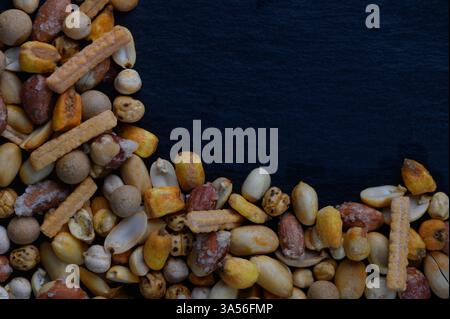 Verschiedene Nüsse und Snacks sind wunderschön auf einer dunklen Oberfläche verstreut und heben ihre verschiedenen Formen und Farben hervor. Dieses lebendige Display erfasst den Stockfoto
