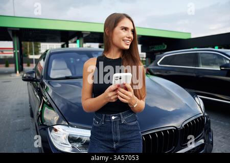 Weißes Smartphone in den Händen. Die Frau ist draußen in der Nähe ihres Autos. Stockfoto