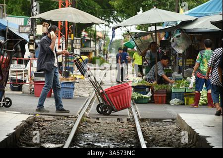 Asiatischer Mann schiebt Gemüse und Gegenstände in einen Plastikkorb auf einem Lastwagen am Bahnhof Mahachai zu seinem Ziel. Stockfoto